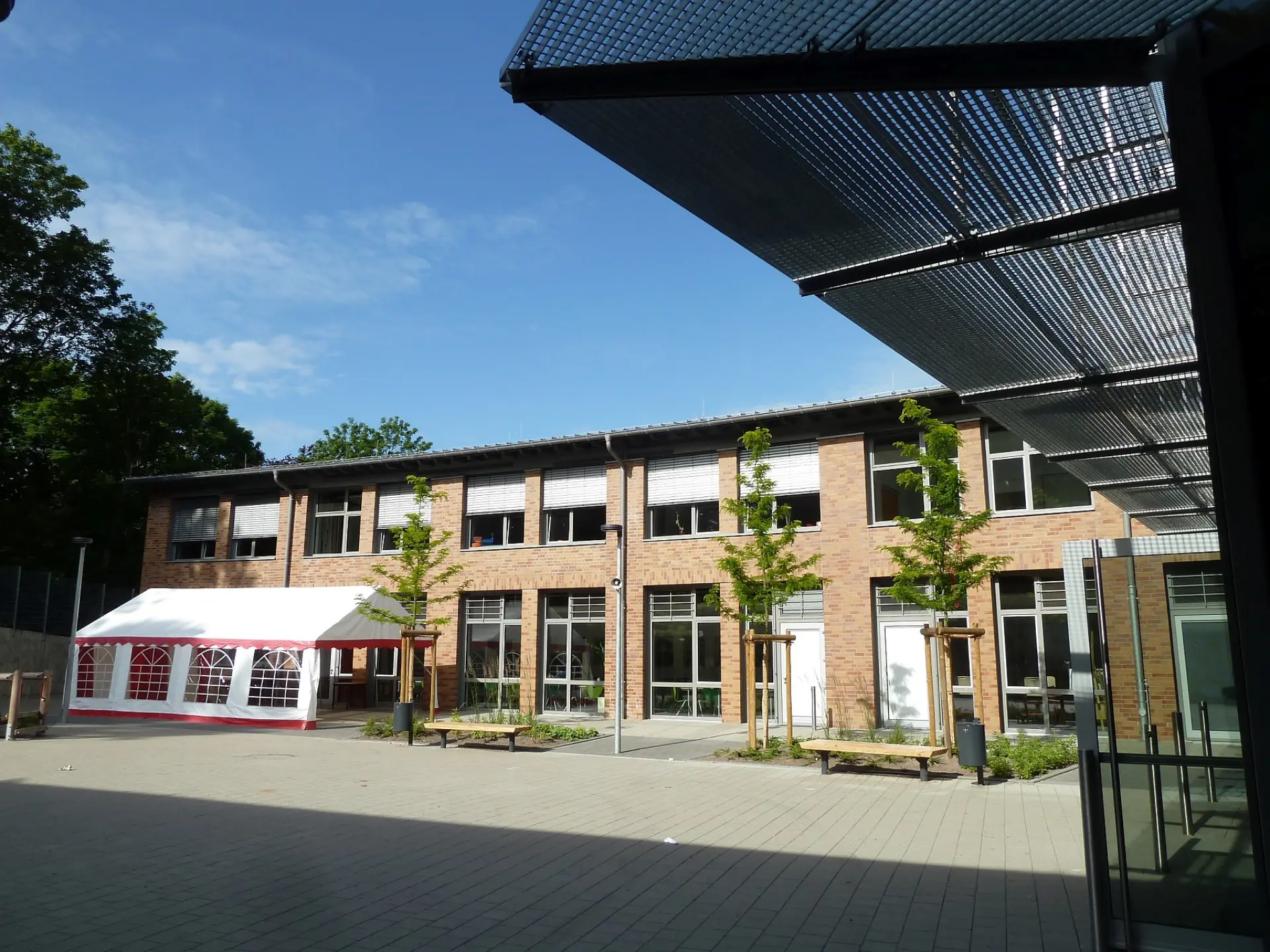Gepflasterter Innenhof der LVR-Gutenberg-Schule mit einem weißen Festzelt, jungen Bäumen und Holzbänken vor der modernen Backsteinfassade