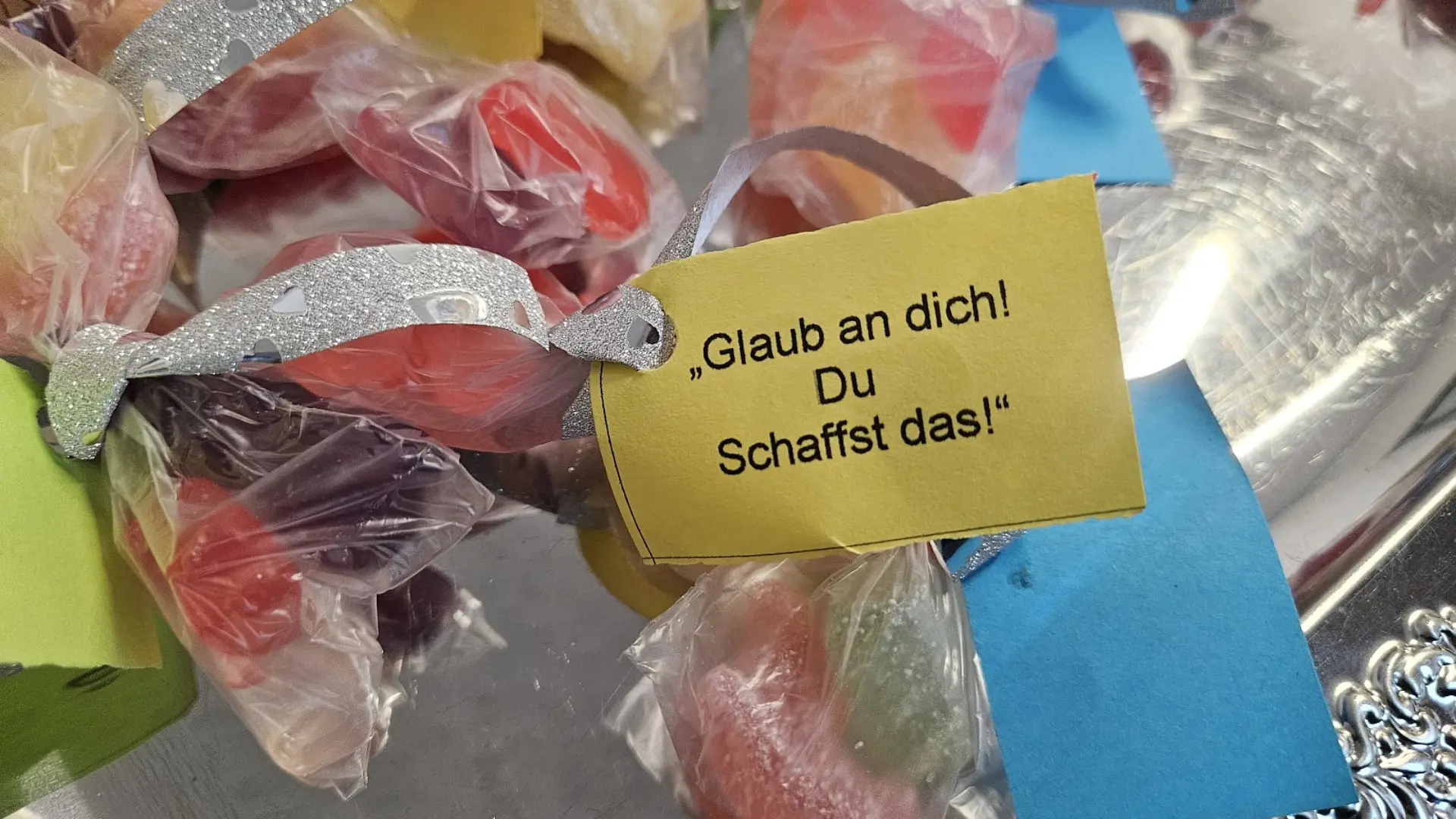 Nahaufnahme von mehreren durchsichtigen Plastiktütchen mit Bonbons drin. Jedes davon ist mit einer Schleife zugebunden und mit einem Zettel mit dem Spruch "Glaub an dich! Du schaffst das!" versehen.